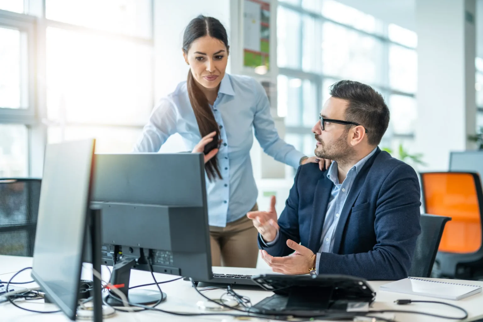 Two colleagues discussing work at a desktop computer