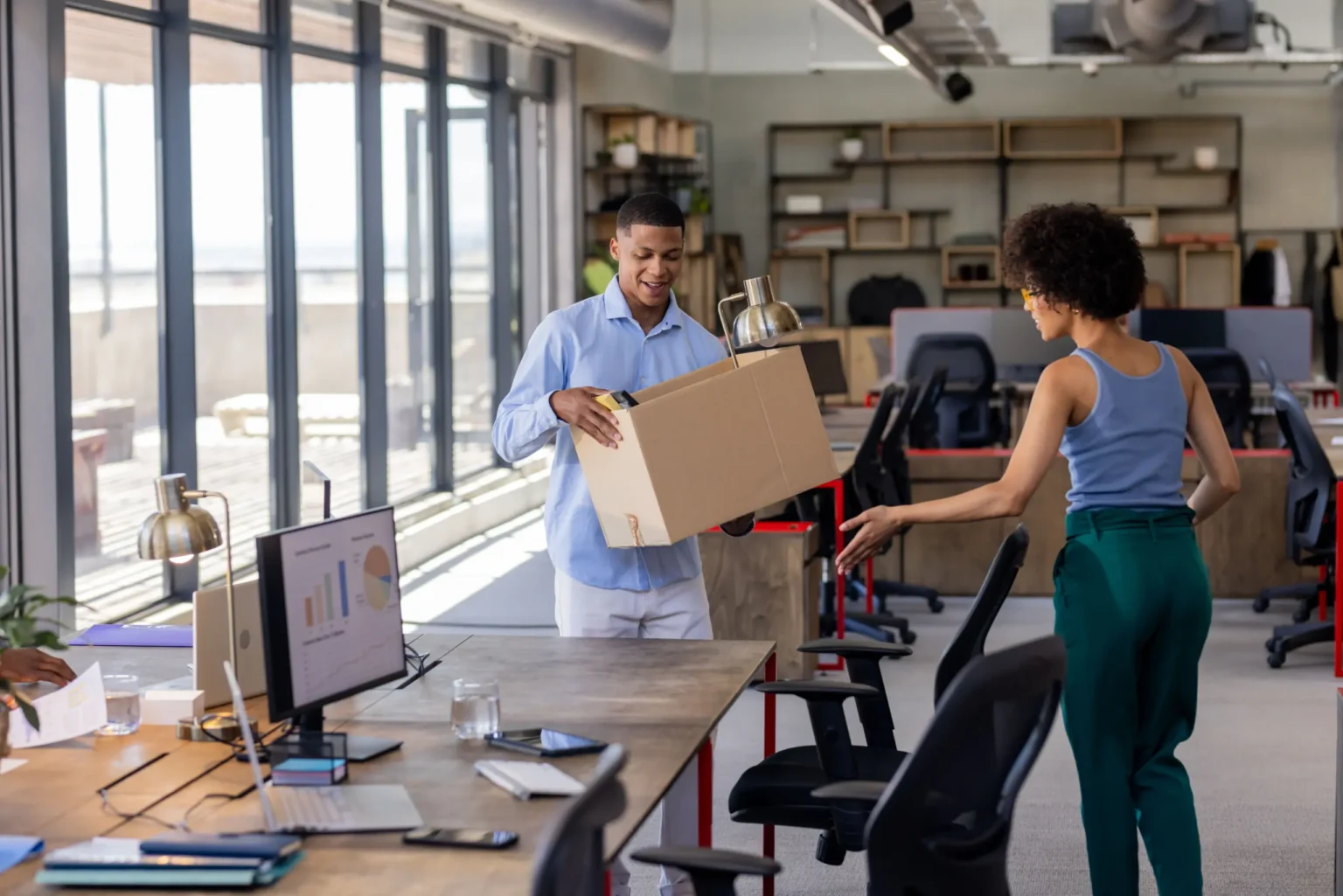 Colleagues packing desk items into a box in an open-plan office