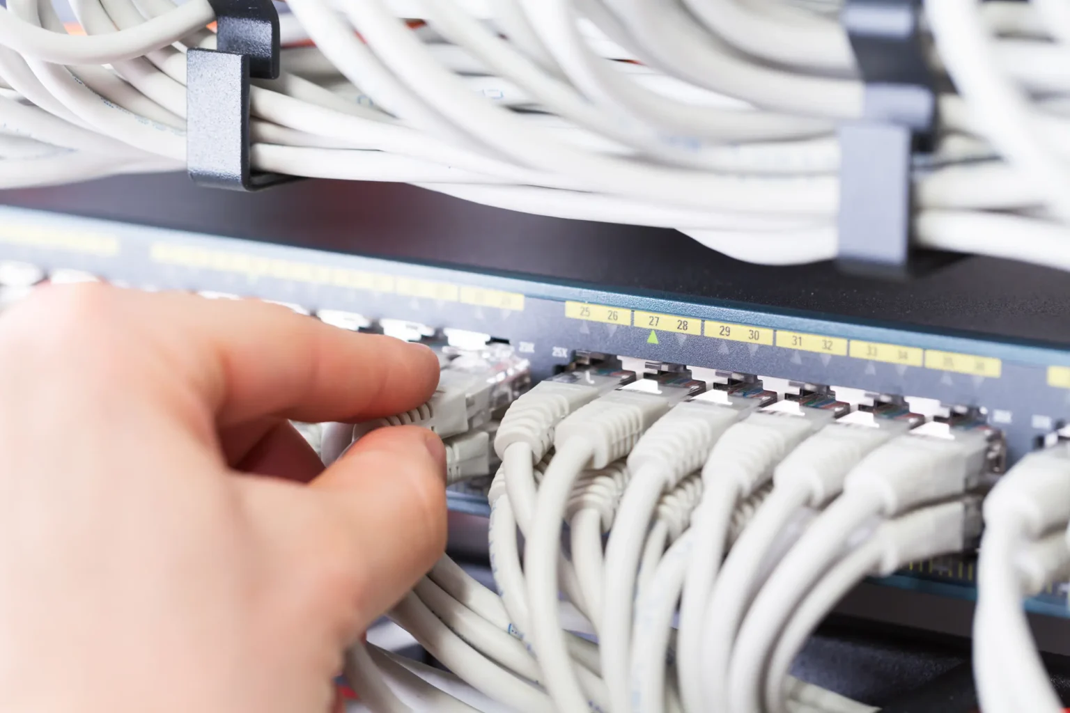 A hand plugging network cables into a network switch