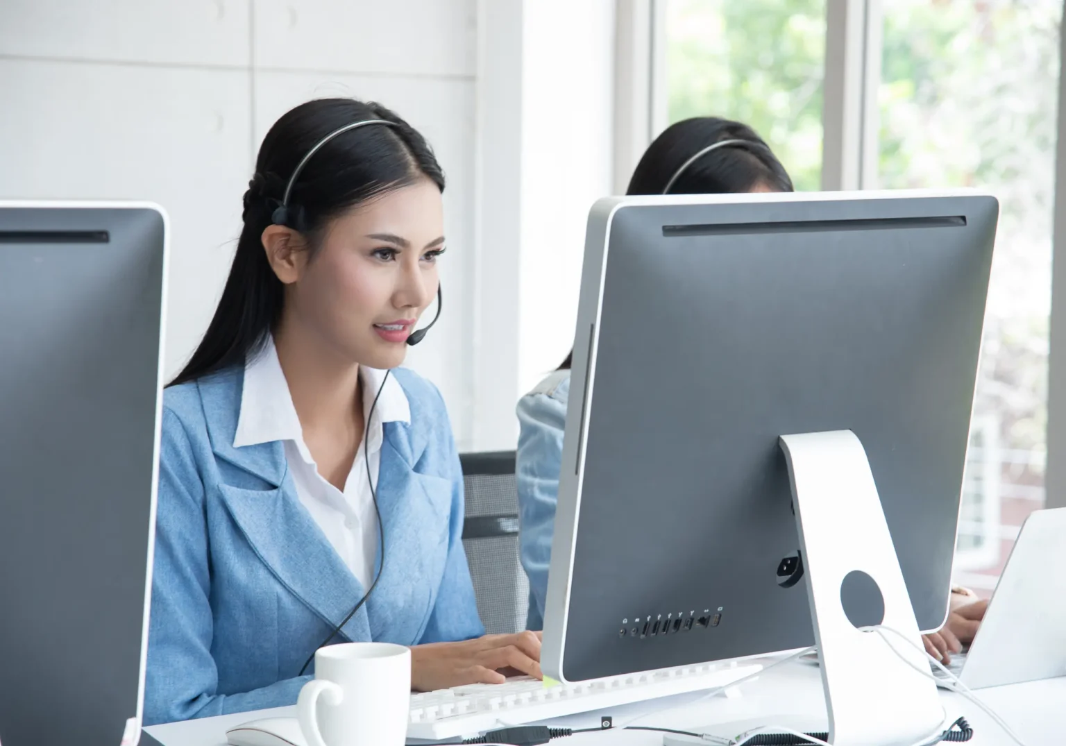 An IT support technician on a headset helping a client at her workstation
