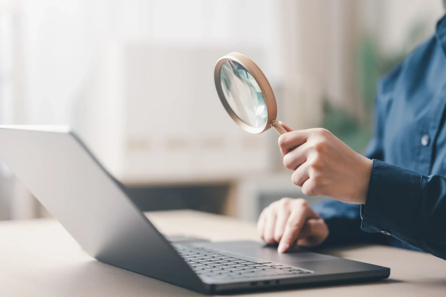 A person holding a magnifying glass while using a laptop