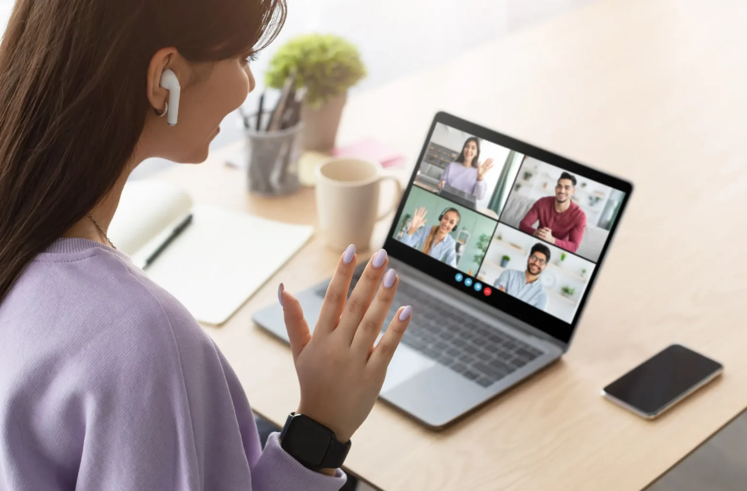 A woman waving to colleagues on a video call on her laptop